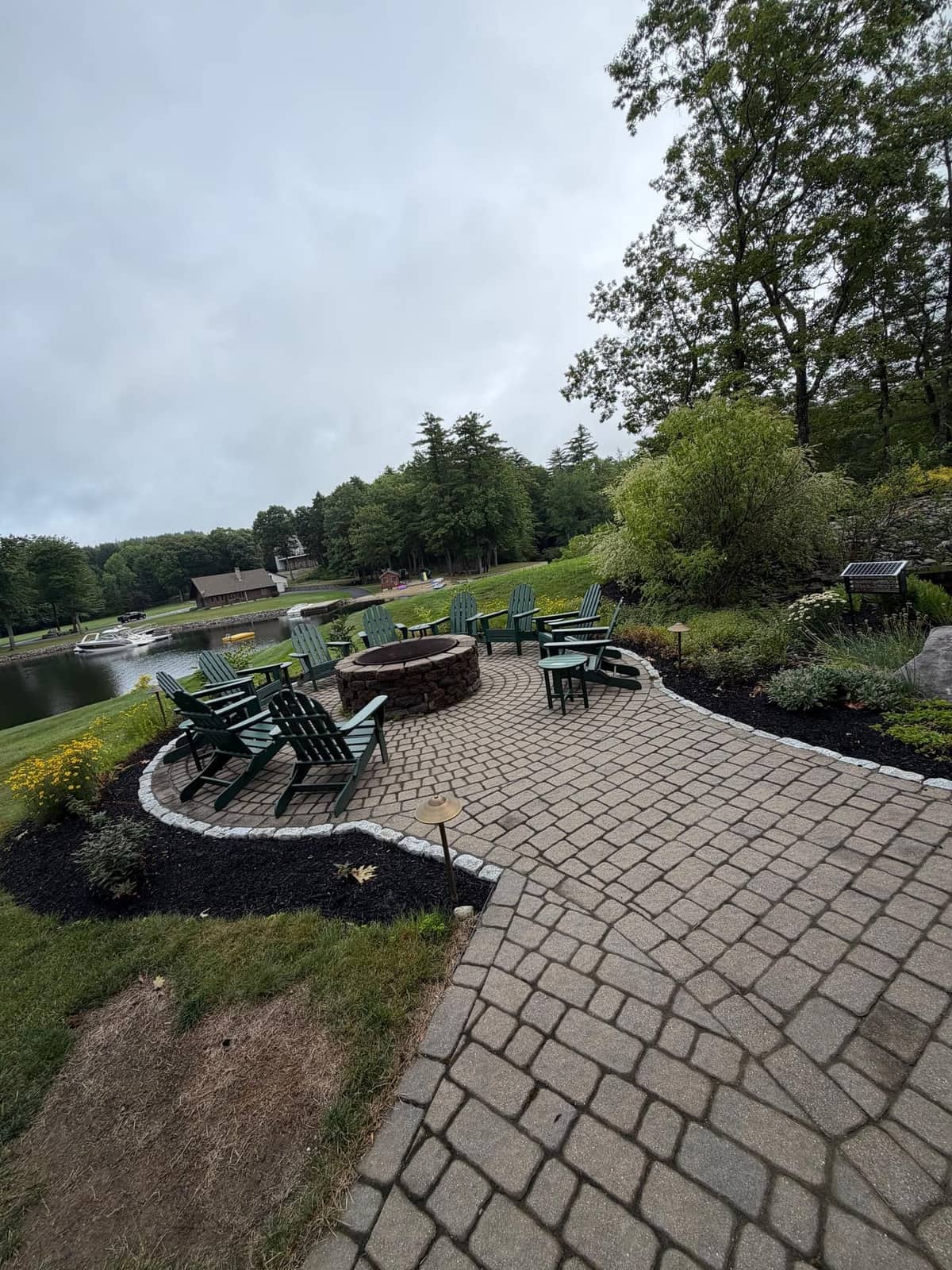 Paver patio with stone fire pit and Adirondack chairs overlooking a lake
