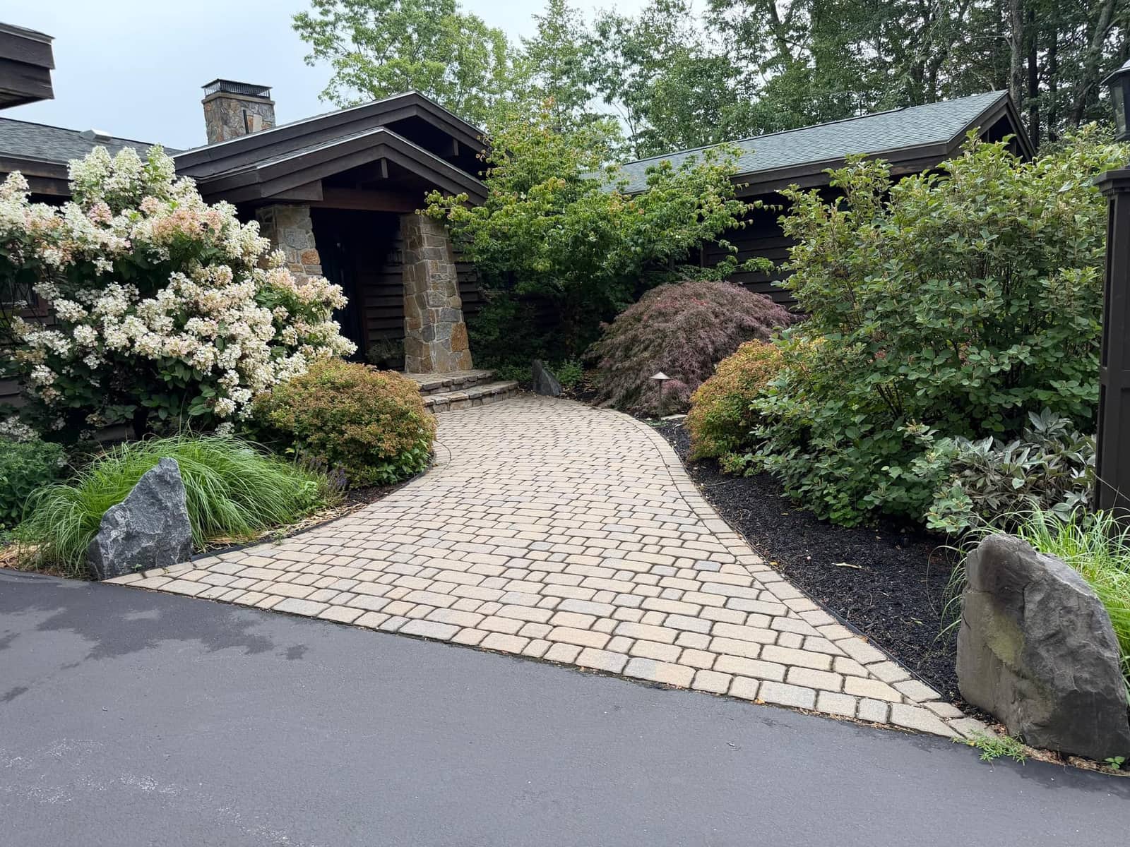 Tumbled paver walkway leading to a craftsman entry through mature plantings