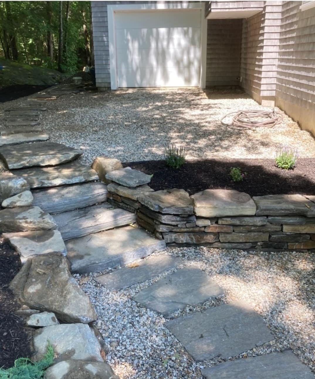 Stacked stone wall and slab steps beside a pea stone courtyard